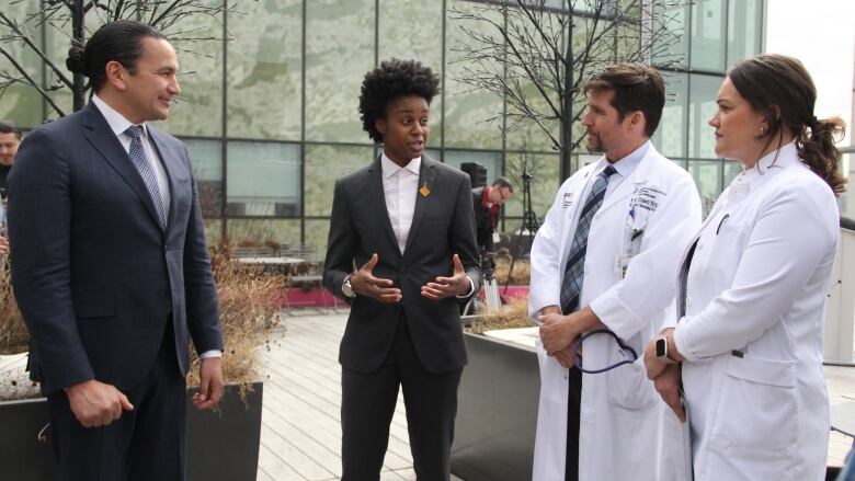 Two people in suits on the left speak to two people in lab coats on the right.