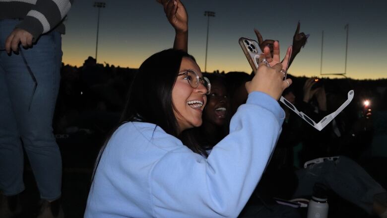 A woman smiles looking up as she takes a photo on her phone.