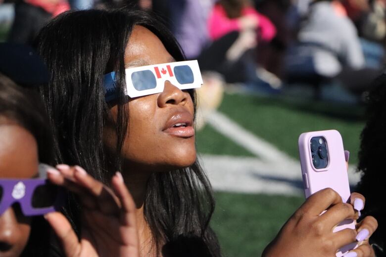 A woman wears eclipse glasses and looks up.