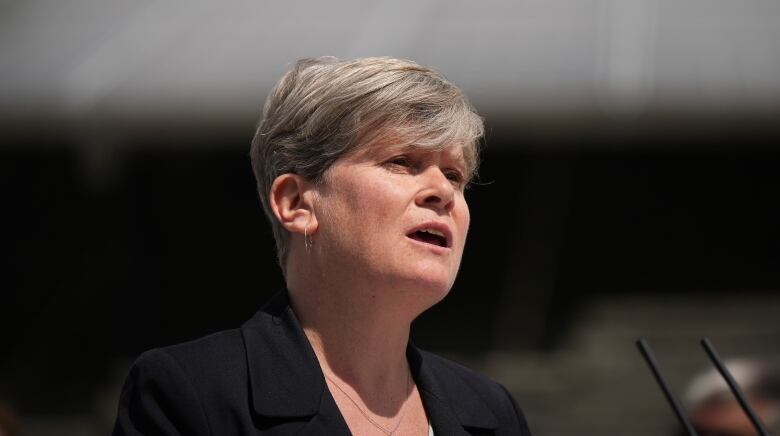 A woman with short hair speaks at an outdoor event.