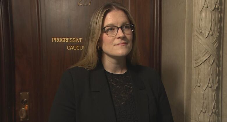 A woman wearing glasses and a suit is pictured looking forward.