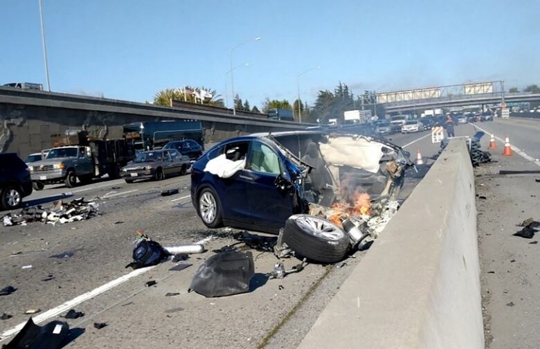 A vehicle is shown with its front section totalled lying against a major roadway barrier. 