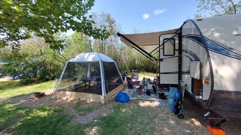 An RV, tent and camp chairs are pictured on a sunny day in an Alberta campsite. 