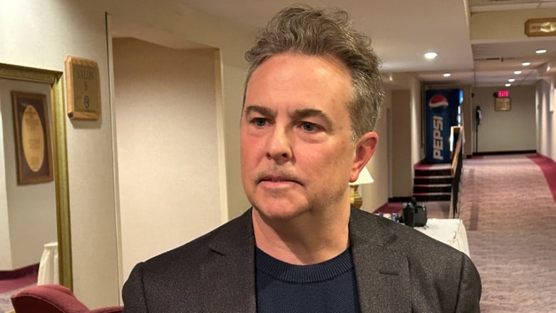 A man wearing a blazer standing in the hallway of a hotel.