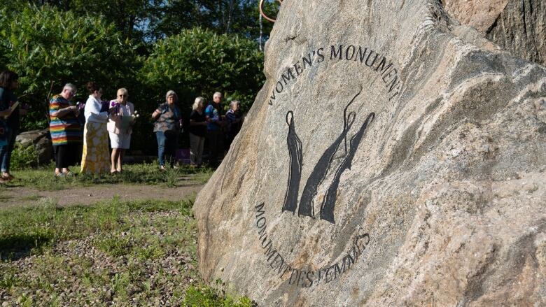 A close up of a women's stone monument. People are lining up in the background.