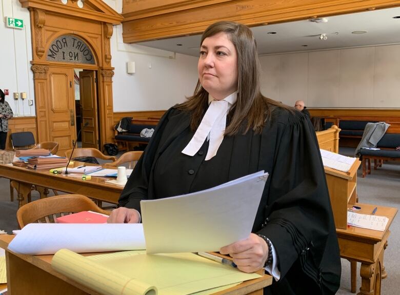 A woman is wearing a black robe and white tie. She is standing over a wooden platform covered in paper. 