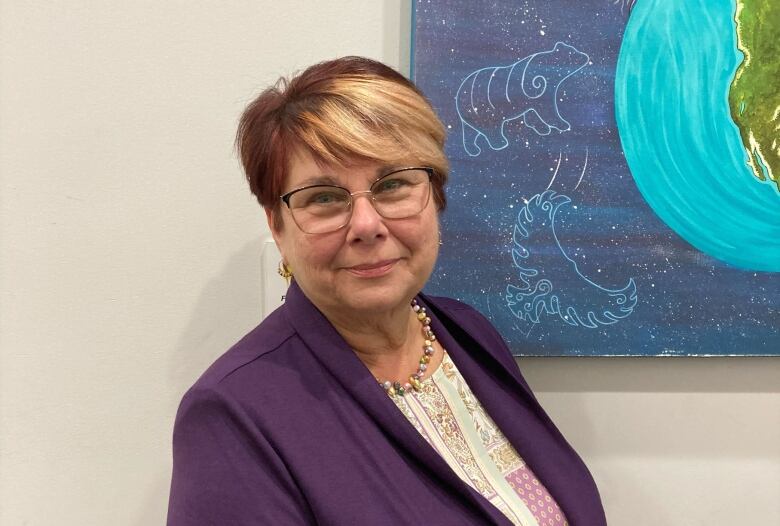 A woman in glasses with short red and blonde hair poses for a portrait.