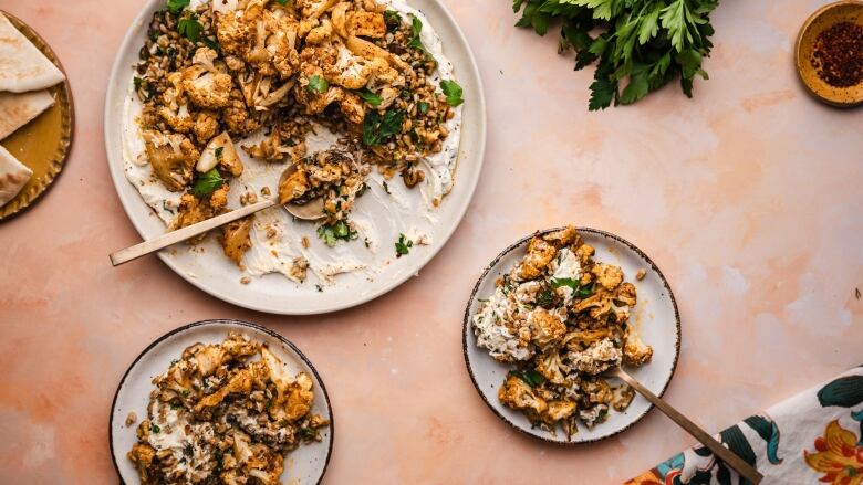 Overhead shot of 2 plates and a serving platter that have a salad with roasted cauliflower, dates and herby farro on top of yogurt.