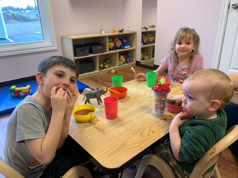 Three children under the age of five eat grilled cheese sandwiches at a small table. 