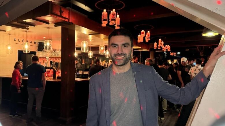 A man smiling with his hand on the wall inside a bar. 