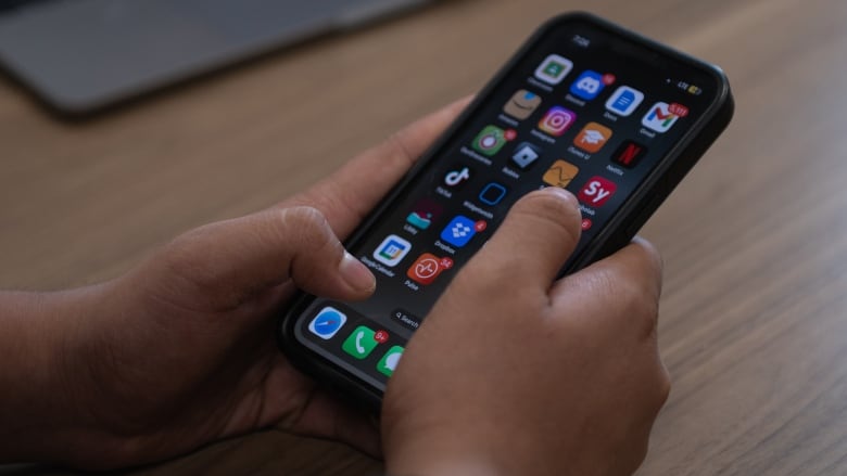 A close-up image of a teen boy holding a smartphone, his thumbs hovering over the apps -- including TikTok and Instagram -- on his home screen.