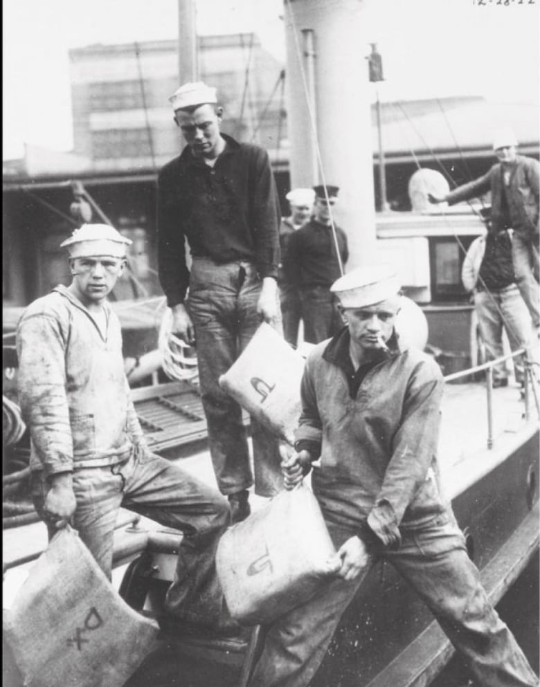 Three coast guard members are seen taking bags of cargo off the deck of a vessel