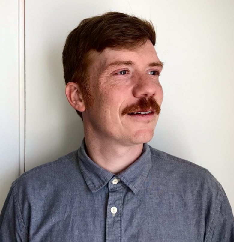 A man in a chambray shirt looks to his left in a portrait photo