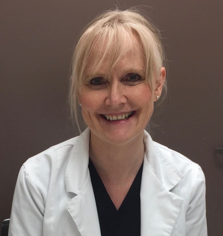 A dentist smiles at the camera, wearing a white lab coat.