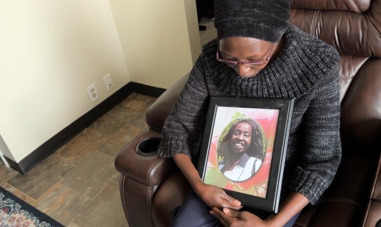 A woman sits on a couch holding a photo of a younger woman. 