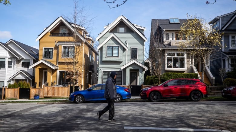 A man in  a hooded sweatshirt walks past  a row of colourful houses