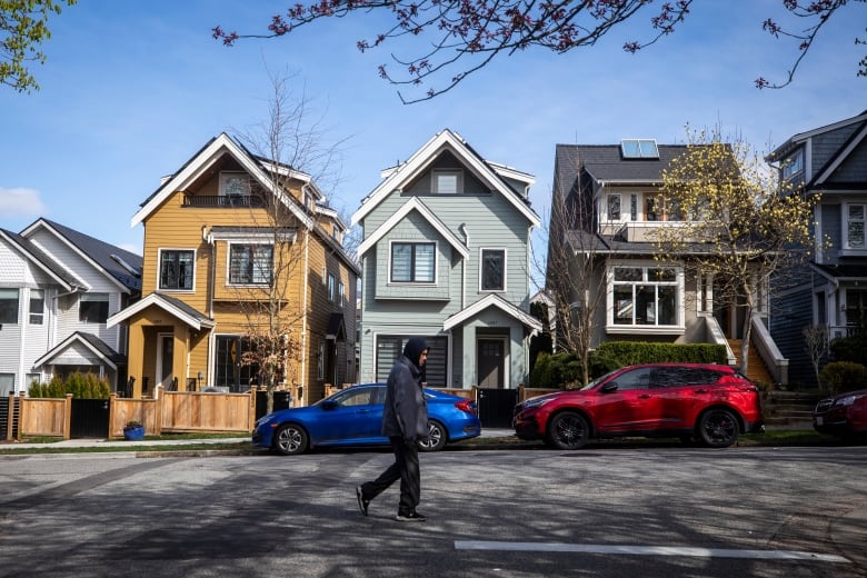 A man in  a hooded sweatshirt walks past  a row of colourful houses