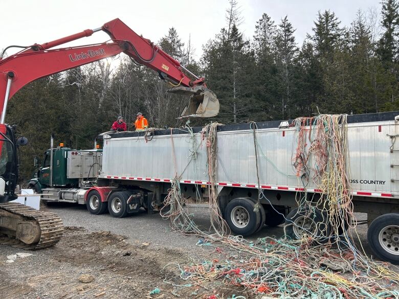 An excavator lifts old fishing rope into a truck.