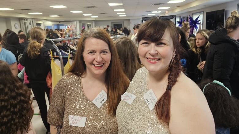 Two women, both wearing gold-sparkled dresses standing in the middle of a crowd. 