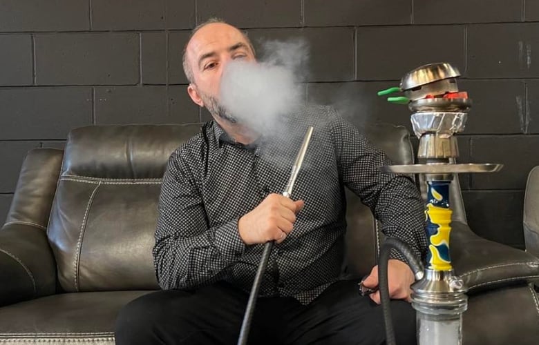 A man sitting on a couch smokes shish through a water pipe.