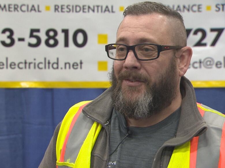 Man with beard and glasses wearing neon yellow safety vest.