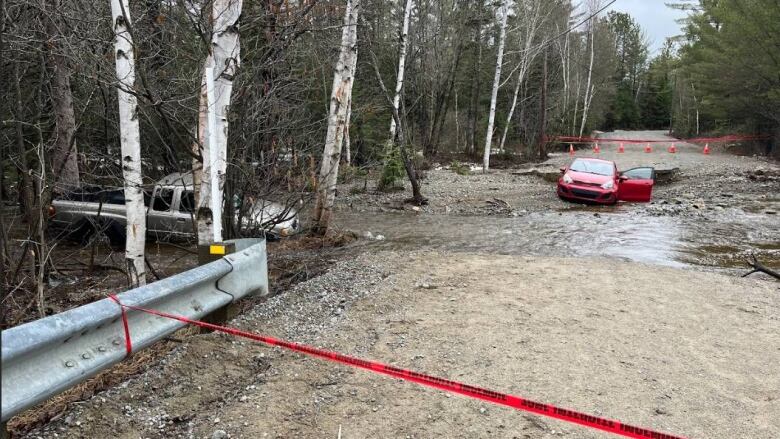 A red car is stuck on a partially flooded dirt road. Red tape closes off the area around the vehicle. 