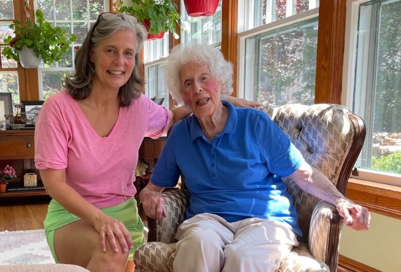 Two women, one older and sitting on a chair, pose for the camera in a well-lit room.