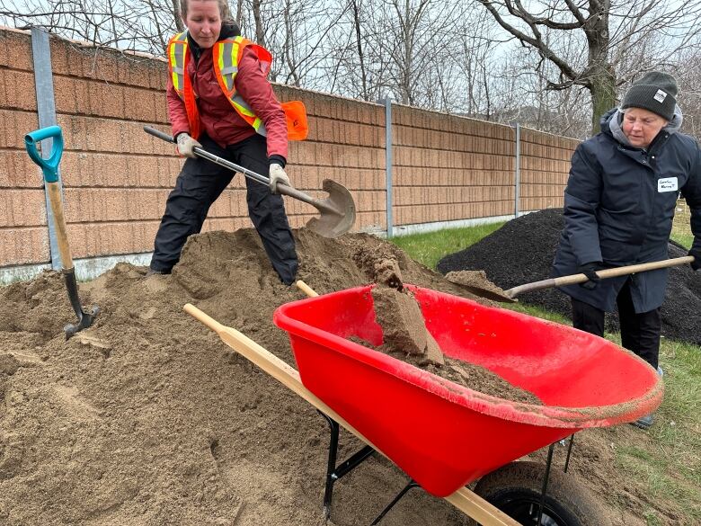 Two Pollinator Roadsides pilot project volunteers shoveling sand into a barrel. 