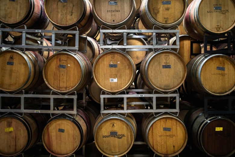 Fifteen stacked wooden wine barrels pictured sitting on metal shelving. 