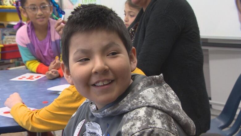 A young child in a grey hoodie smiles.