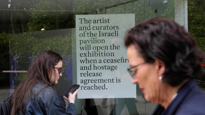 Two women are shown standing by a sign that is posted on a door calling for a ceasefire.