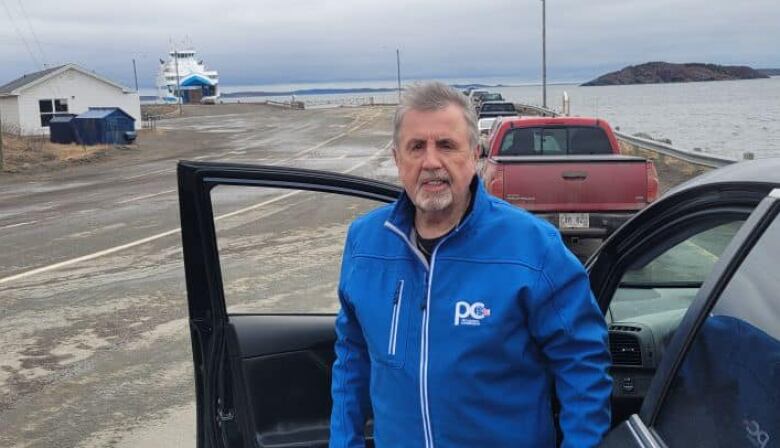 A man in a blue jacket standing outside a car.