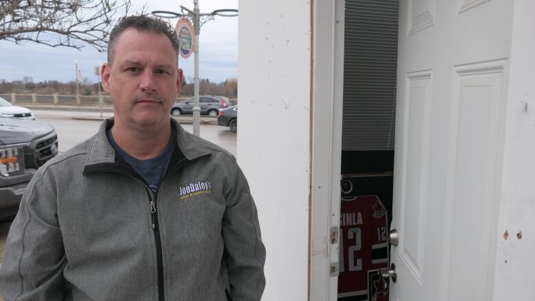 A man stands beside a door that is partly open. He has a frustrated expression.