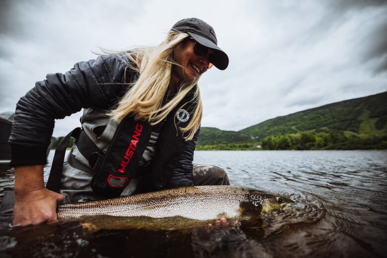 A woman with blonde hair holds a large fish in water. 