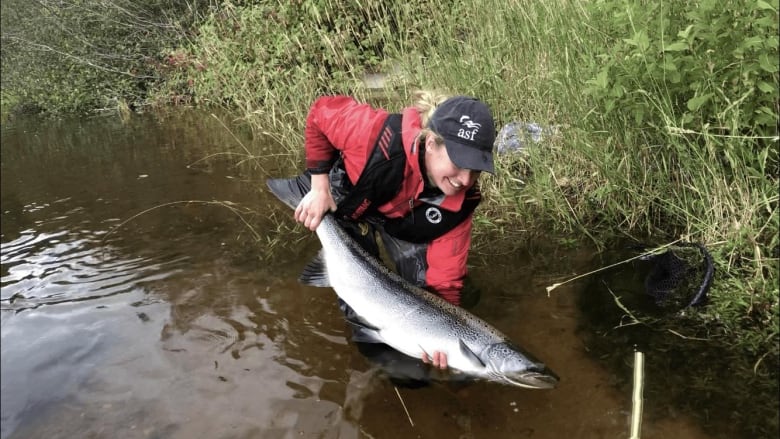 A blonde woman holding a large fish in a river. 