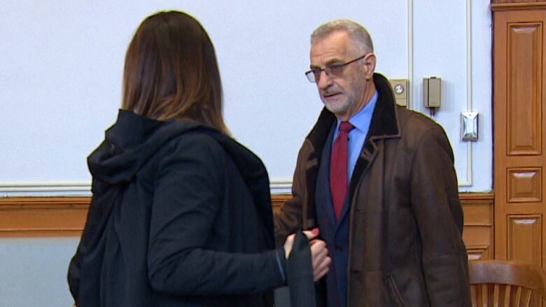 A grey haired man is wearing a brown suede jacket and is carrying a brief case. 