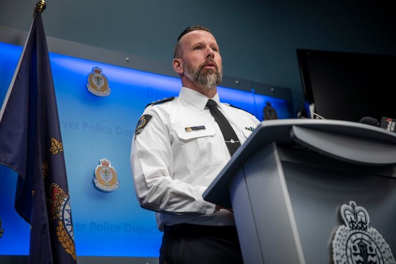 A police officer wearing a white shirt and black tie stands at a podium.