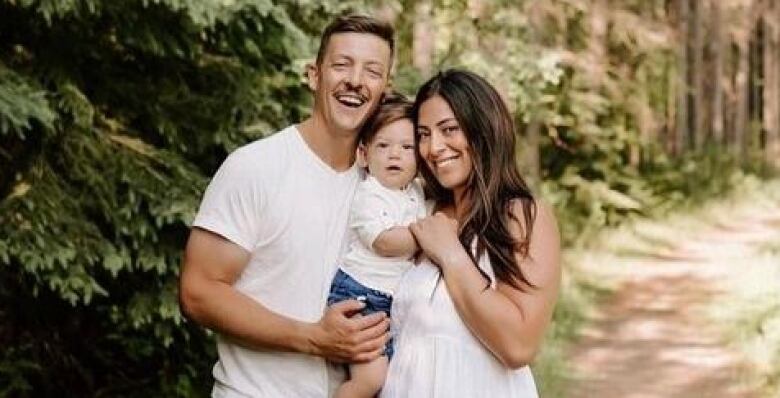 A man and woman are seen smiling and holding a baby between them.