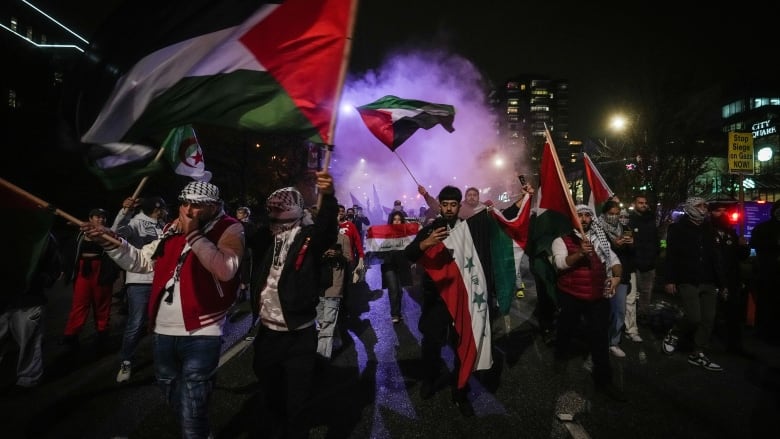 People wave Palestinian flags as smoke bombs are set off during a demonstration in support of Palestine, in Vancouver, on Thursday, October 19, 2023.