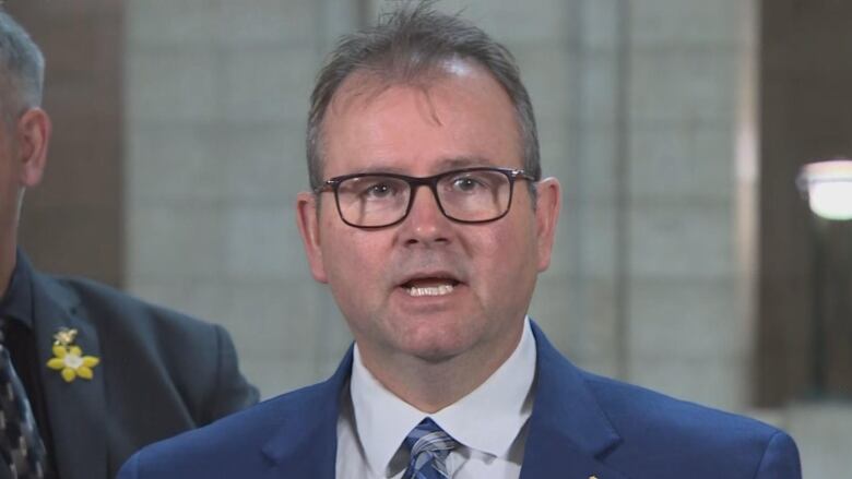 A man wearing glasses and a suit and tie is pictured.