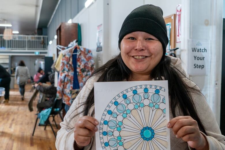 A person wearing a beanie holds up a colouring sheet.