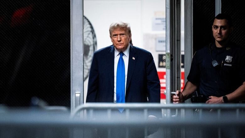 A man in a dark suit with a blue tie walks through security outside a courthouse.