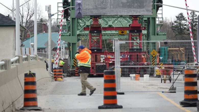 Workers in high-visibility clothing walk past a fence and pylons on a closed bridge under construction.