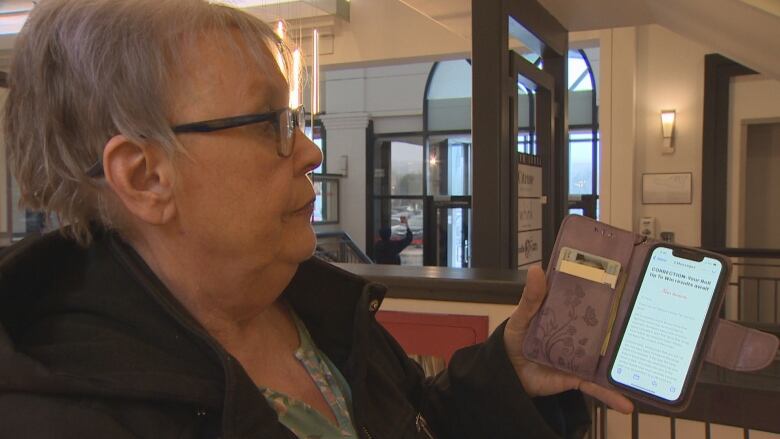 A woman holds up a smartphone with an email on screen.