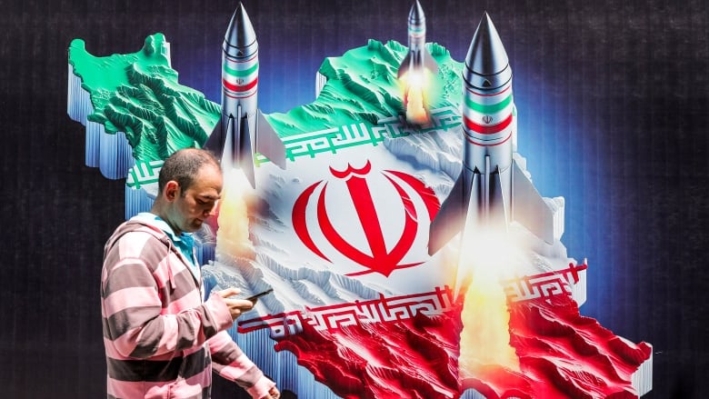 A man in Tehran walks past a banner depicting missiles launching atop a representation of a map of Iran.