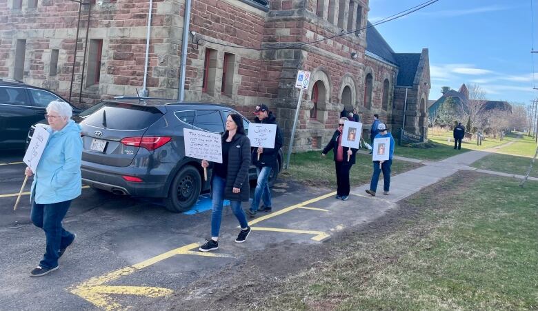 People carrying signs calling for justice for Tyson MacDonald walk outside a stone-clad courthouse.