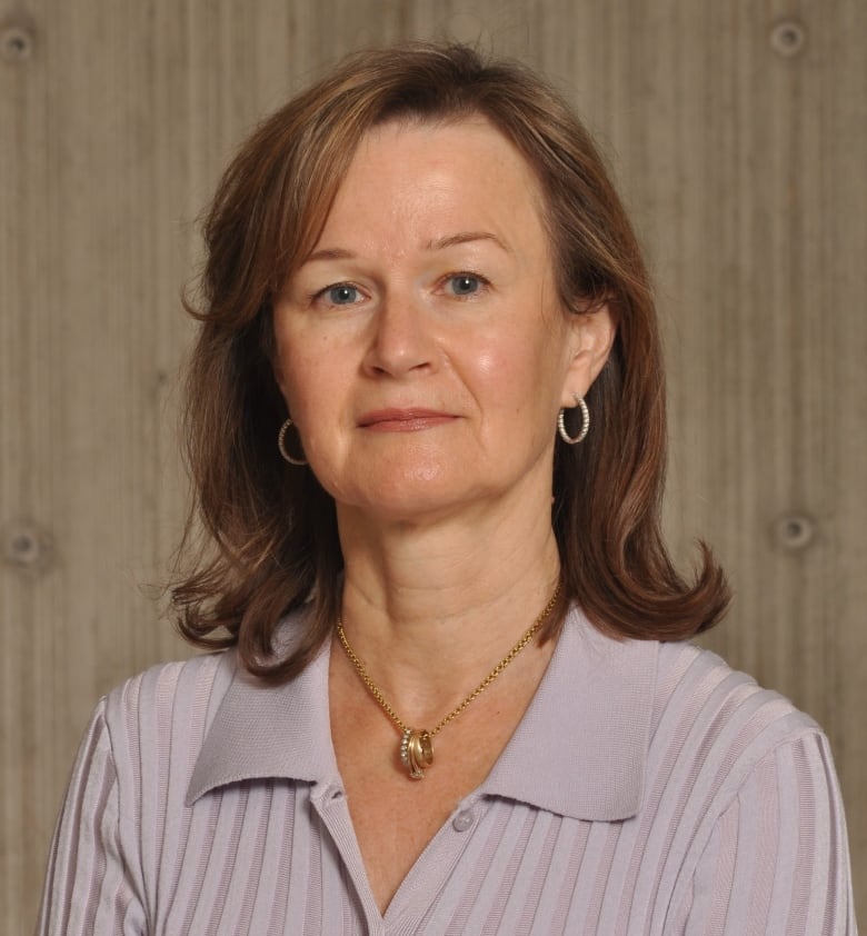 Alix Howlett is wearing a mauve v-neck sweater and necklace and looking directly at the camera in this headshot