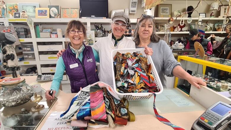 three women pose holding a basket of brightly coloured neck ties