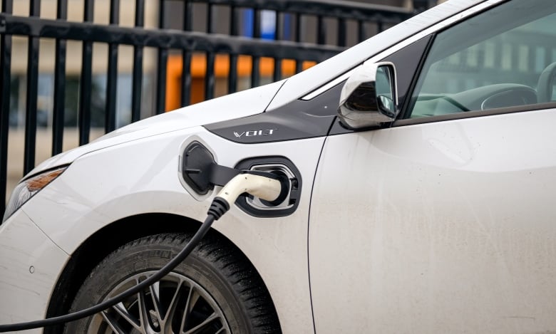 A charger is plugged into the side of a white electric vehicle.