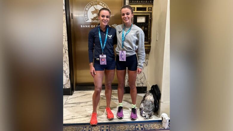 Two people wearing athletic attire stand in front of elevator doors, smiling.